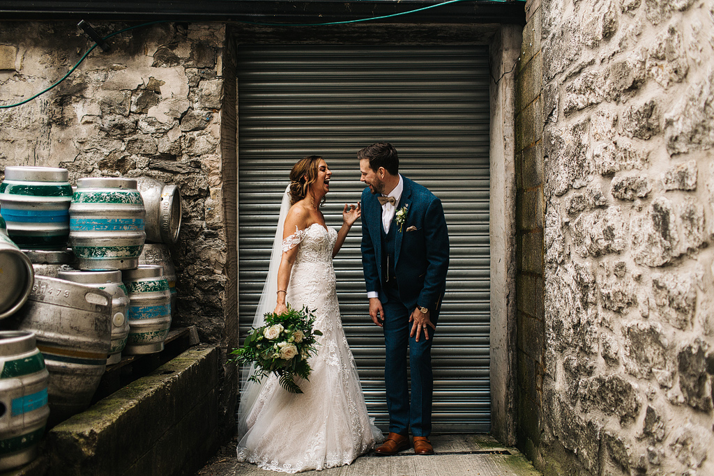 bride and groom laughing by beer barrels at a brewery wedding
