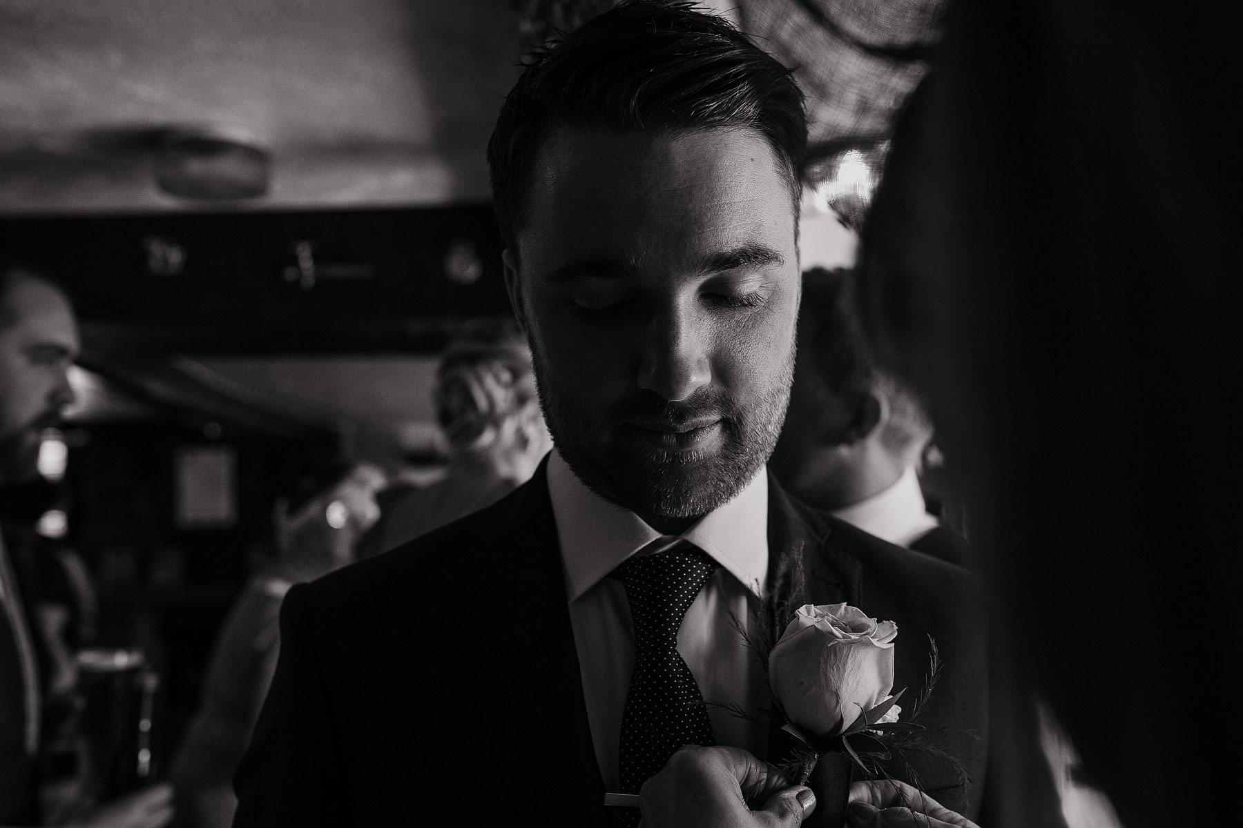 balck and white photograph of a groom havig his flower pinned to his jacket