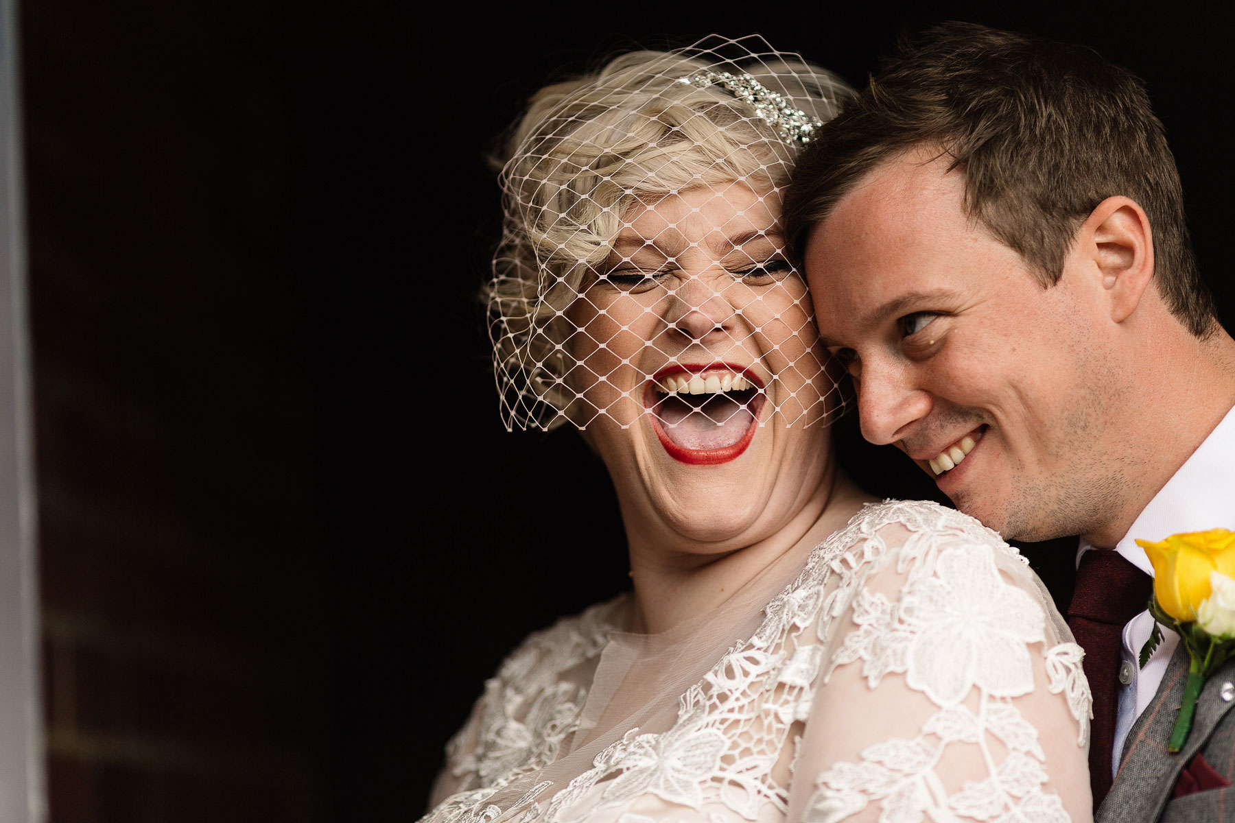 a bride wearing a birdcage veil laughing with red lips
