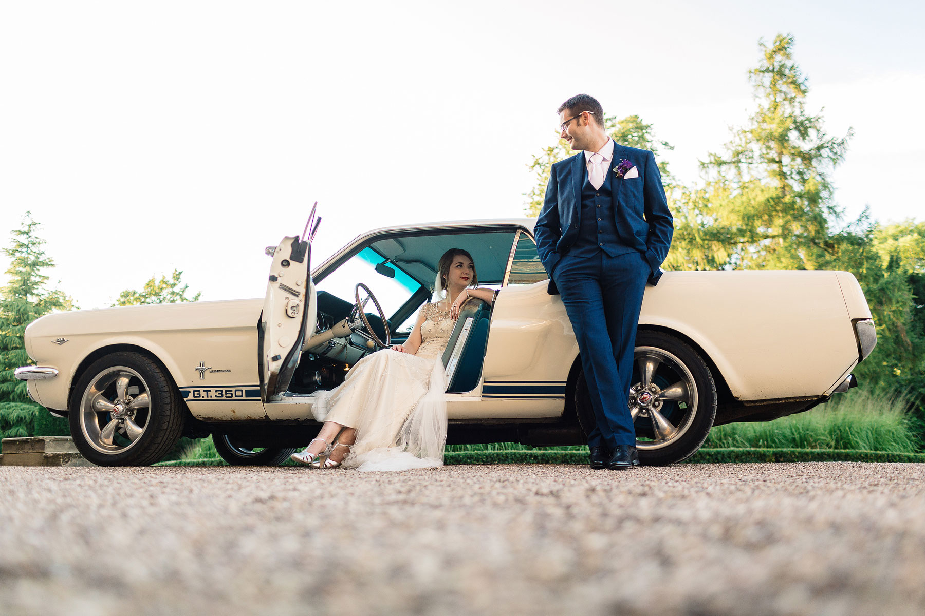 bride and groom stood by a mustang