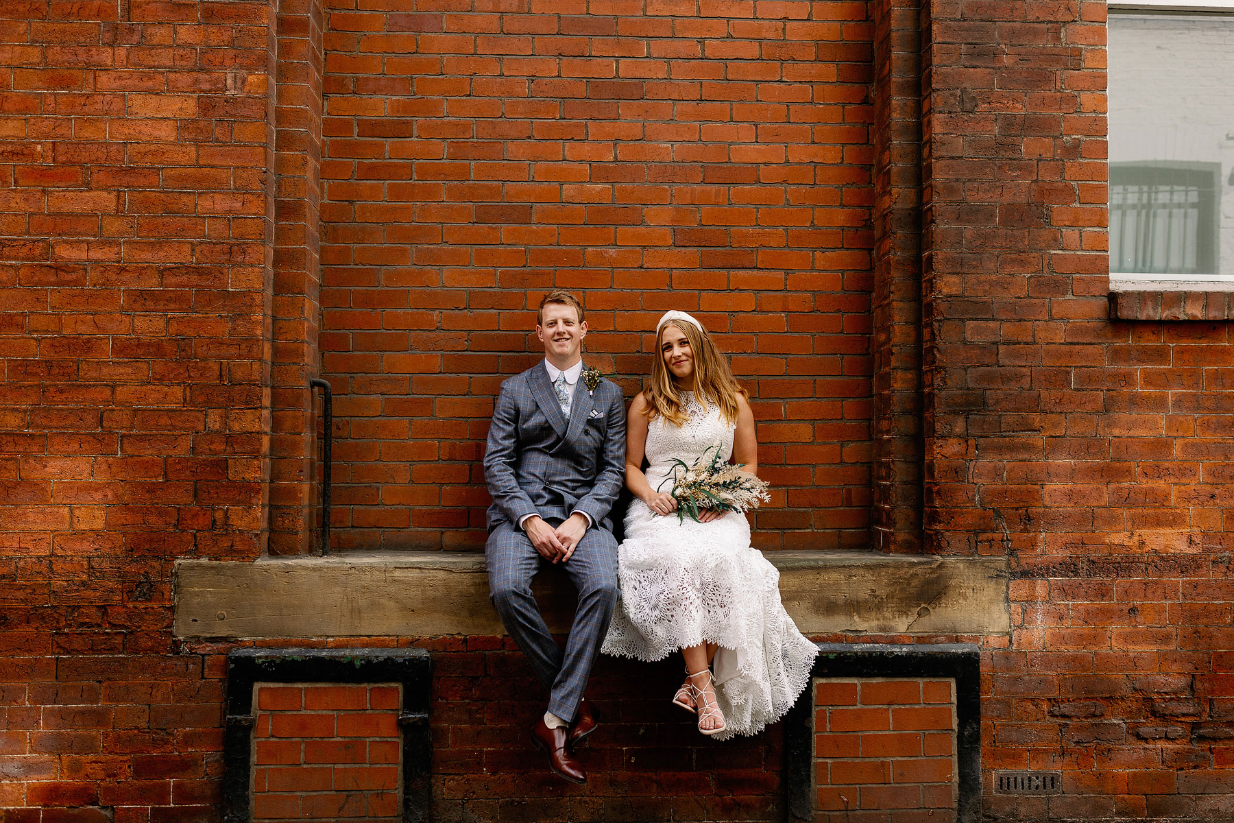fun bride and groom portrait of a couple sat on a wall