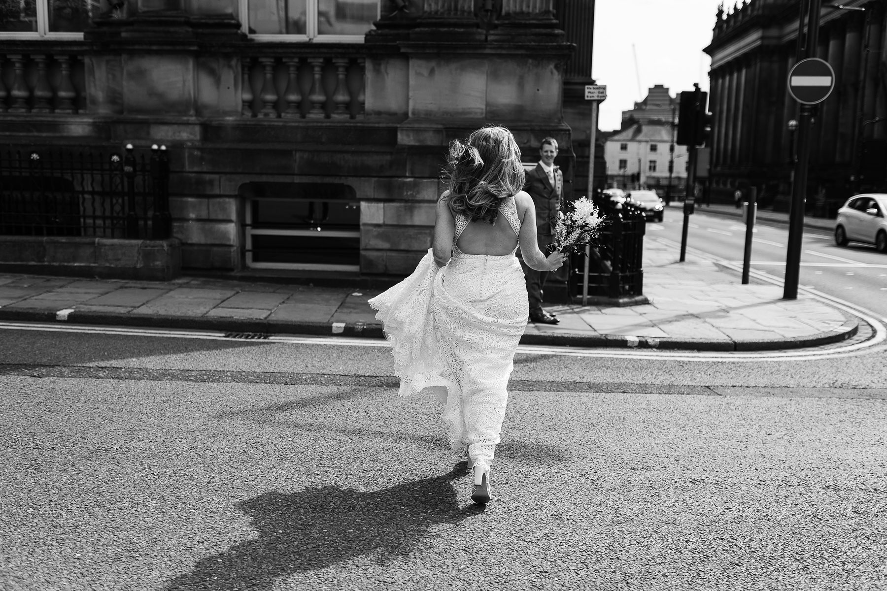 bride crossing the road with her wedding dress flowing behind her