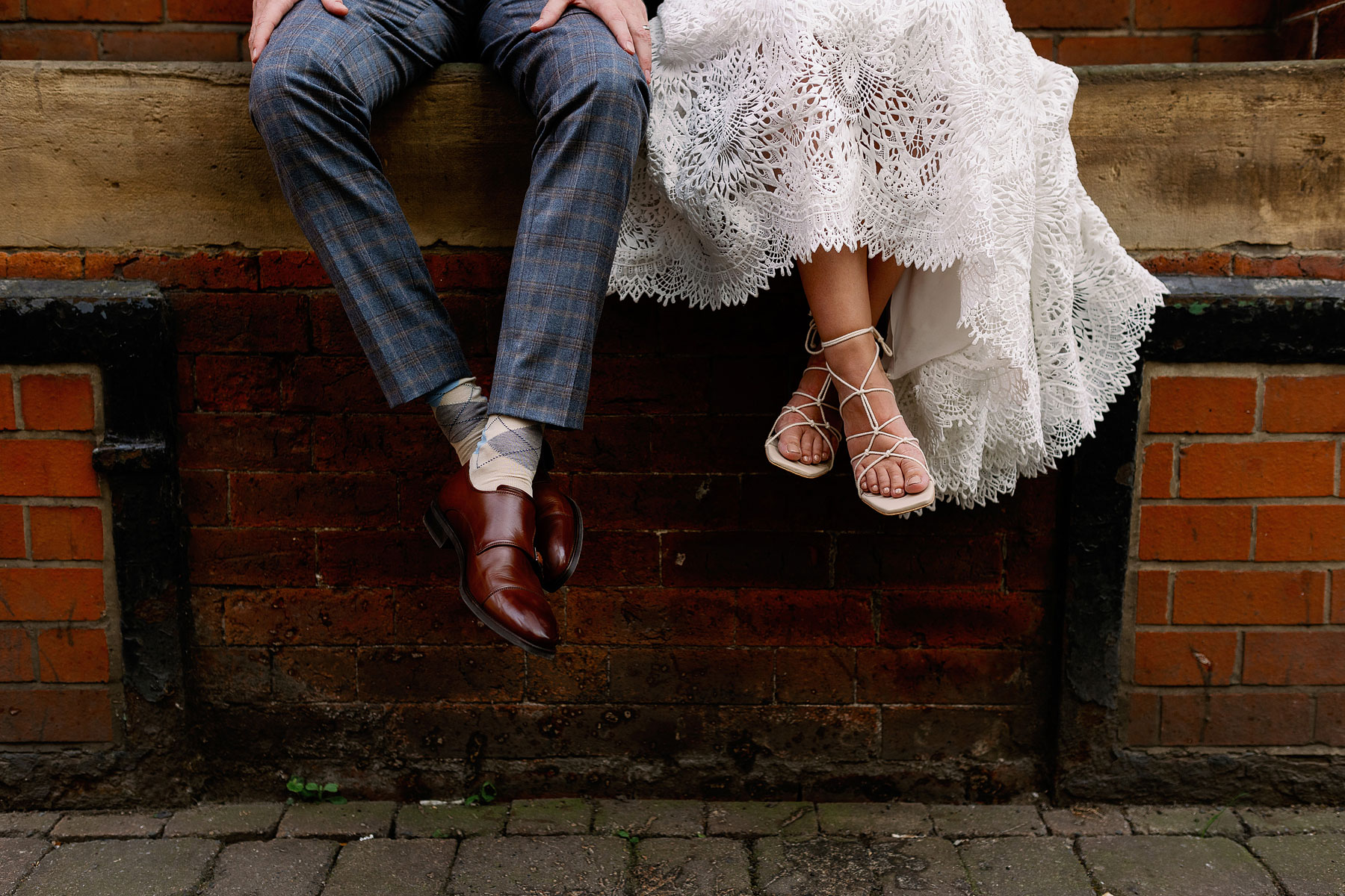 Bride and groom sat with their feet hanging off a wall