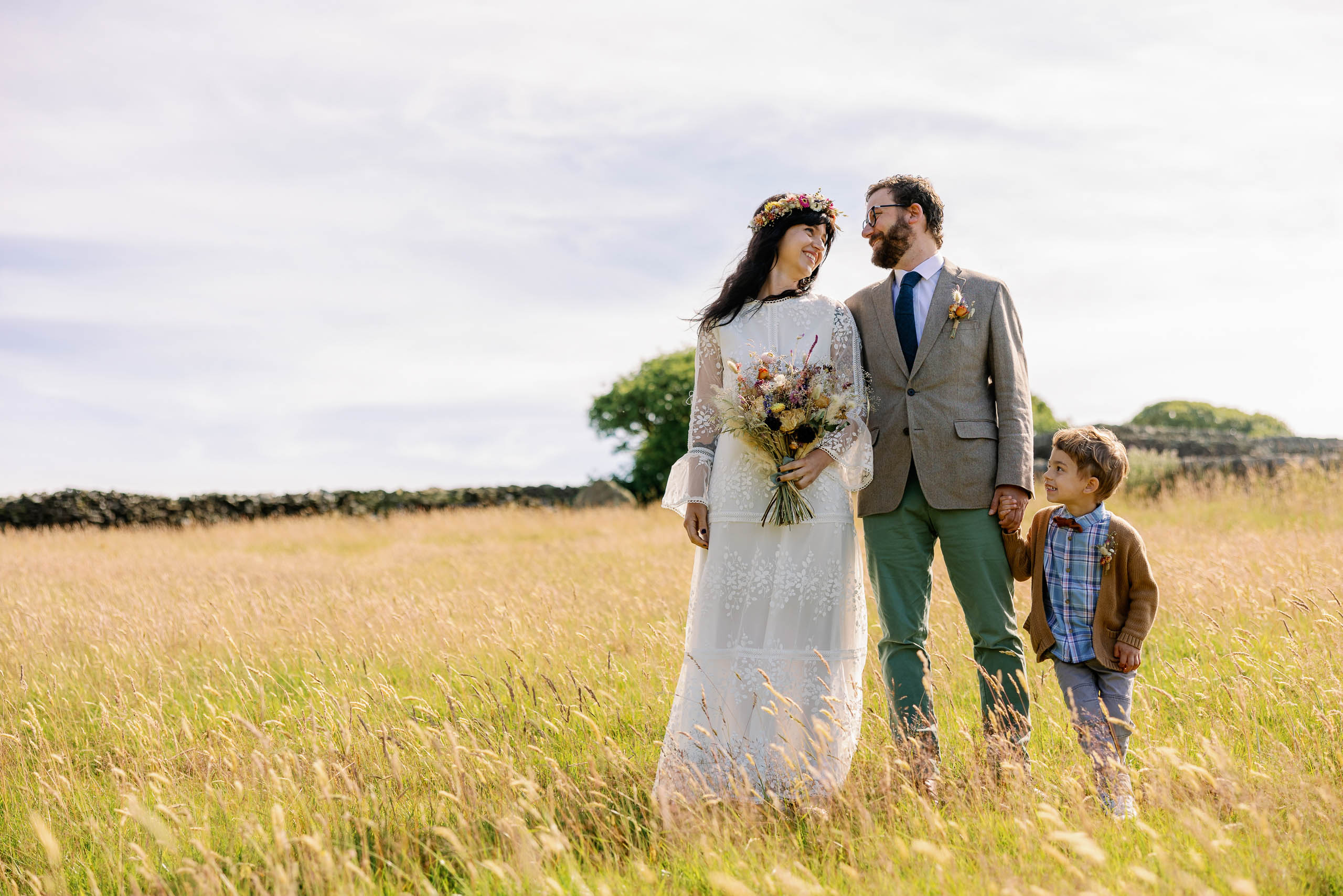 A Boho wedding couple stood in a field of long grass at their Haworth Wedding Blessing