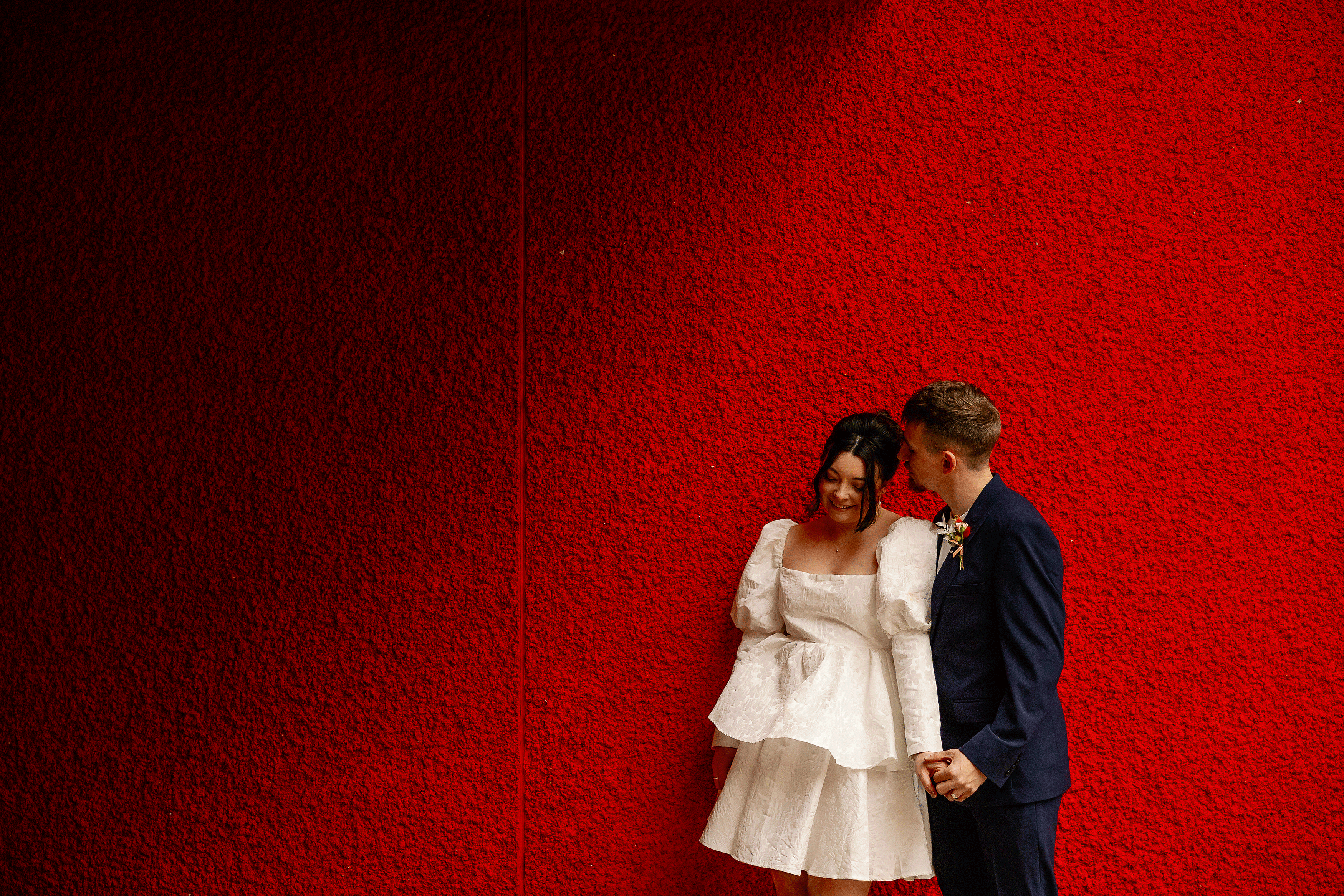 a bride and groom holding hands with a red wall as the backdrop