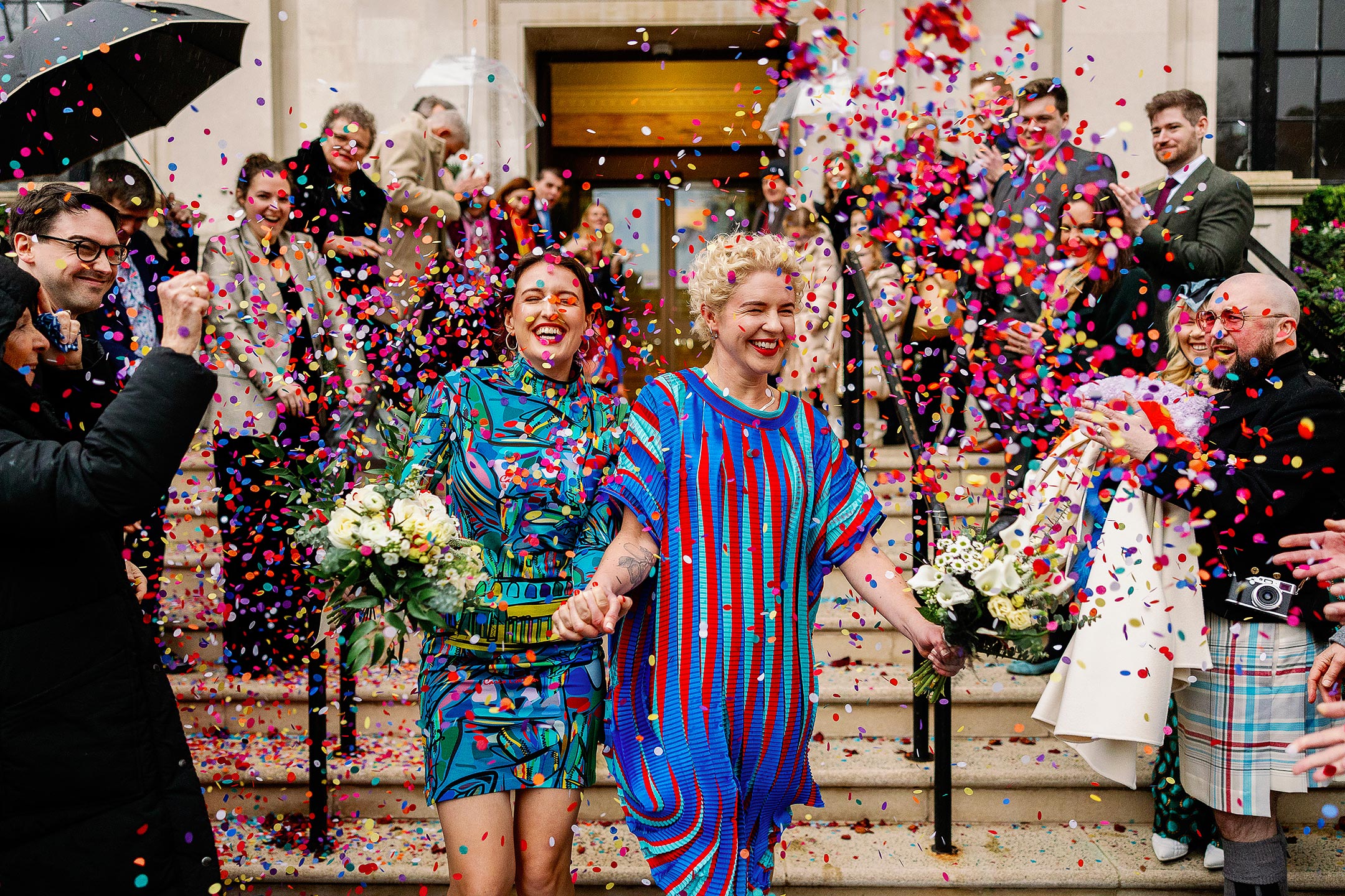 same sex couple in colourful wedding dresses leaving islington town hall to loads of confetti